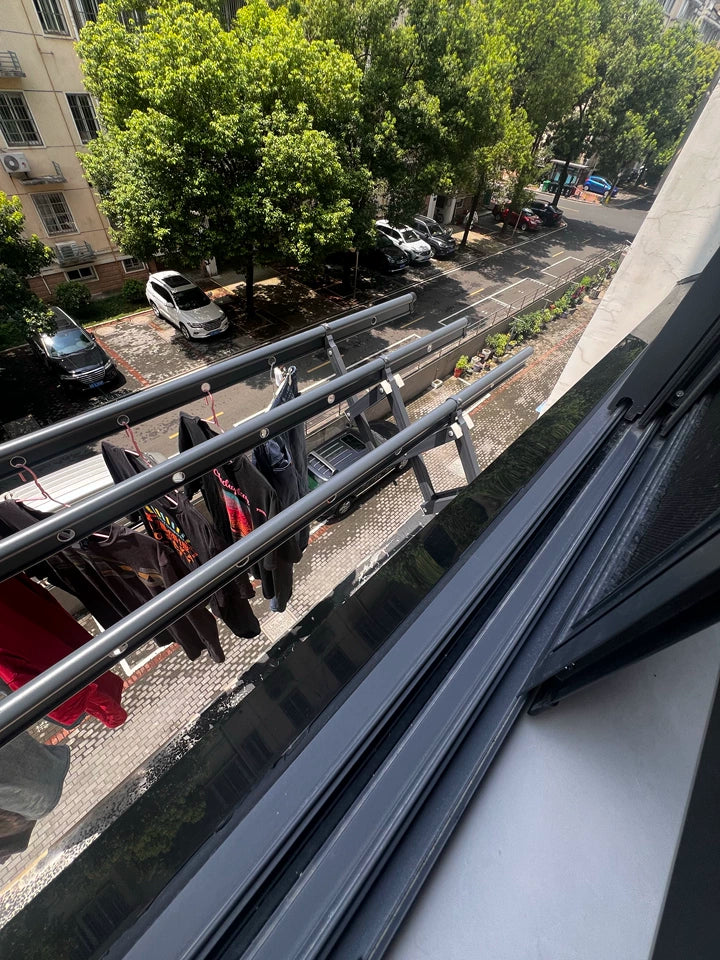 Wall-mounted drying rack fully extended and holding laundry, installed outside a window overlooking the street.