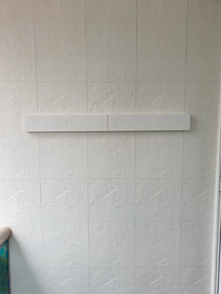 EaseRack foldable clothes airer completely folded against the wall, blending seamlessly with a tiled balcony surface.