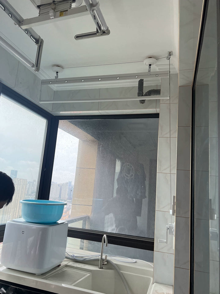Manual ceiling-mounted clothes drying rack installed above a balcony sink near large windows.