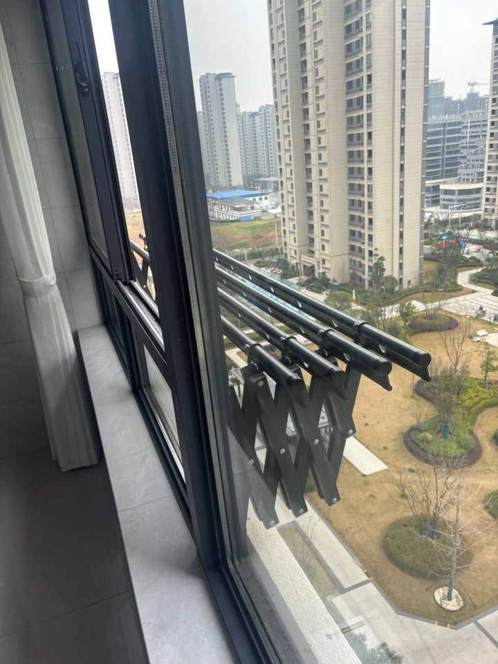 EaseRack wall-mounted retractable drying rack is extended outside a modern apartment window, offering a view of the surrounding buildings and outdoor space. The rack is designed for efficient drying in limited spaces while providing easy access.