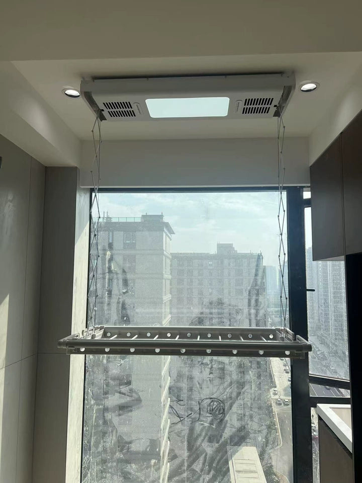 Easerack electric clothes drying rack is mounted on the ceiling in a modern room, with natural light streaming through large windows offering a cityscape view. The rack is suspended and features an integrated light, perfect for indoor clothes drying.