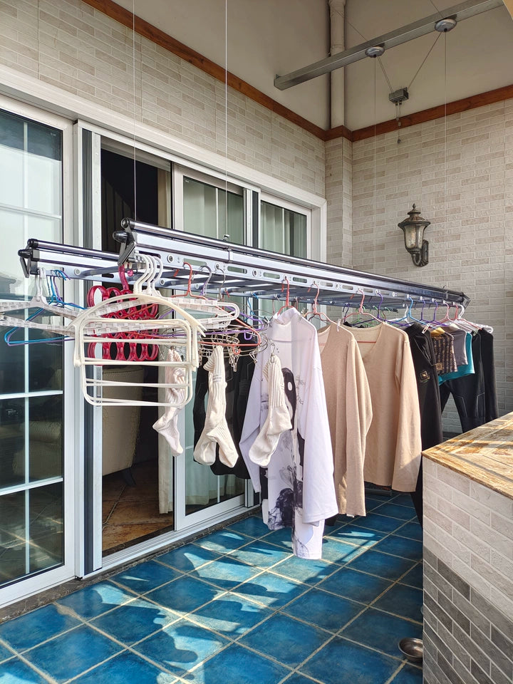Square tube hand crank clothes drying rack fully loaded with clothes on a residential balcony.