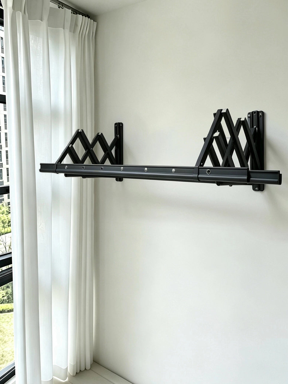 Real customer installation of an EaseRack wall-mounted retractable drying rack on an indoor wall beside a window.