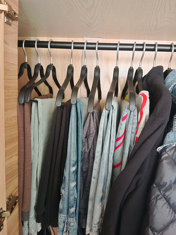 Black no-mark clothes hangers on a wardrobe rail holding shirts, jackets, and outerwear