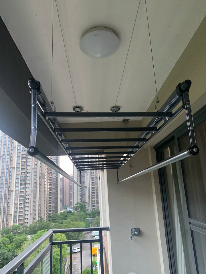 Manual pulley clothes drying rack installed on outdoor balcony with city view.