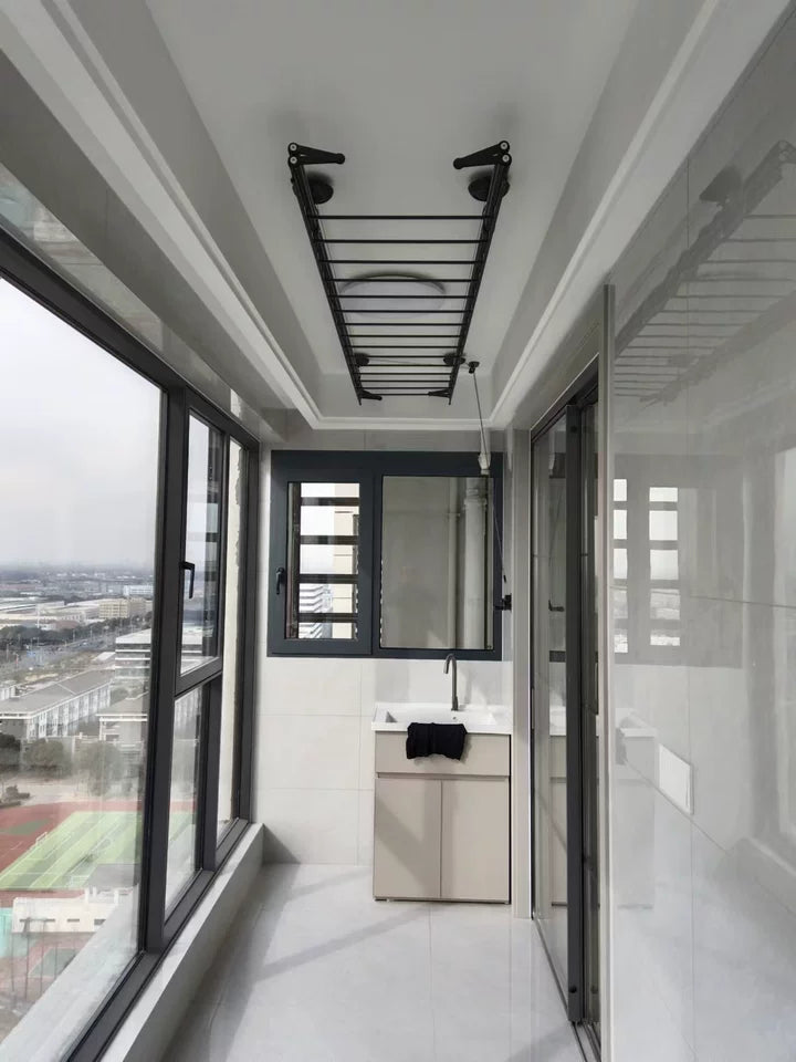  A completed installation of the Hand Winch Clothes Drying Rack in a bright and spacious room with large windows. The rack is mounted on the ceiling, ideal for indoor clothes drying.