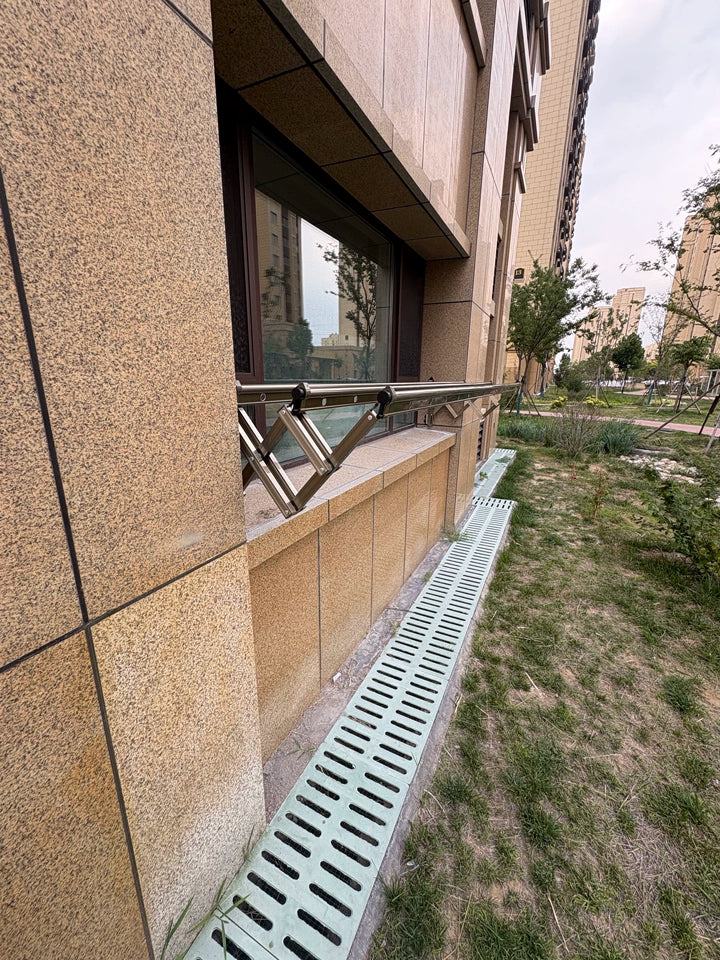 Retractable clothes drying rack mounted at ground-level outside a residential window, blending with modern building facade.