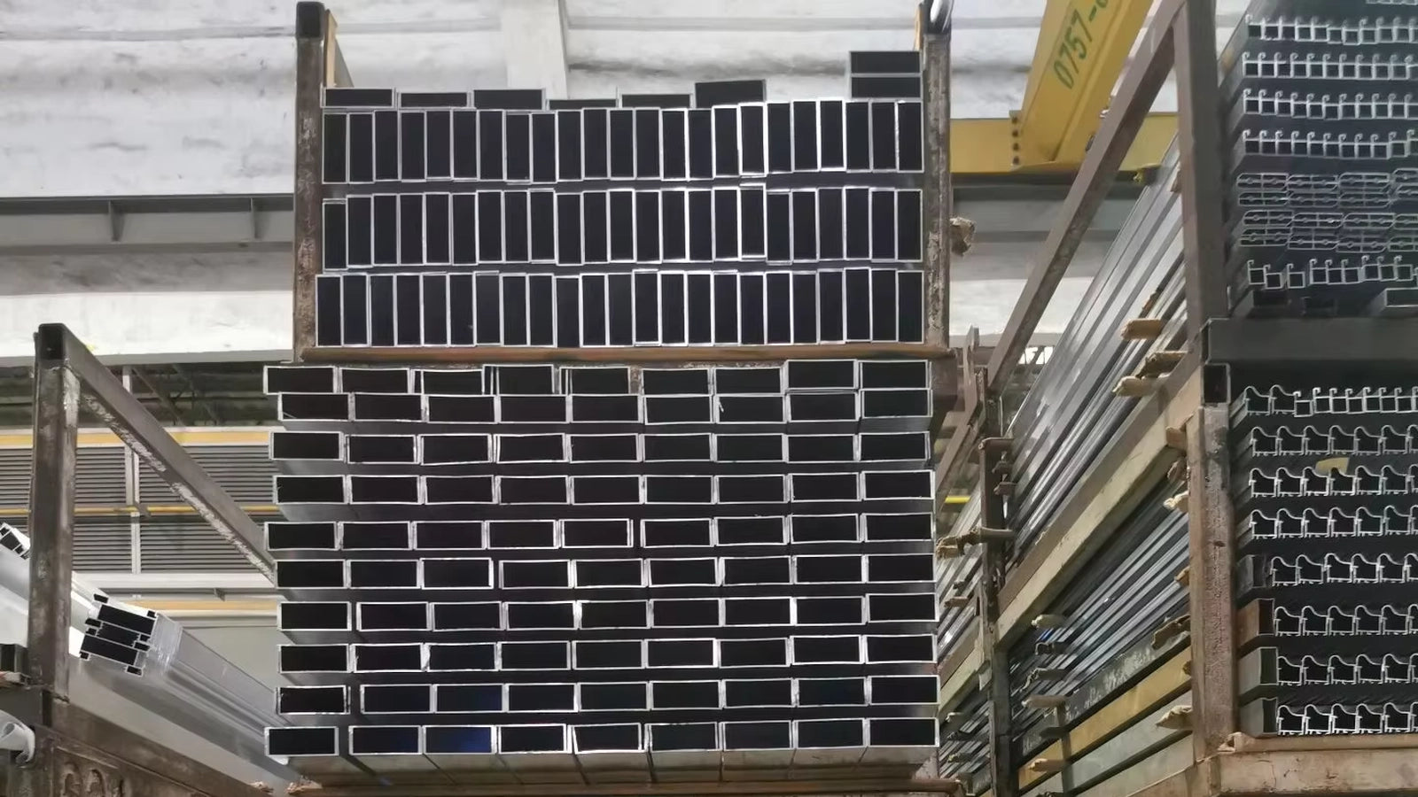 Stacked aluminum profiles stored on industrial racks inside the factory, prepared for manufacturing and production.