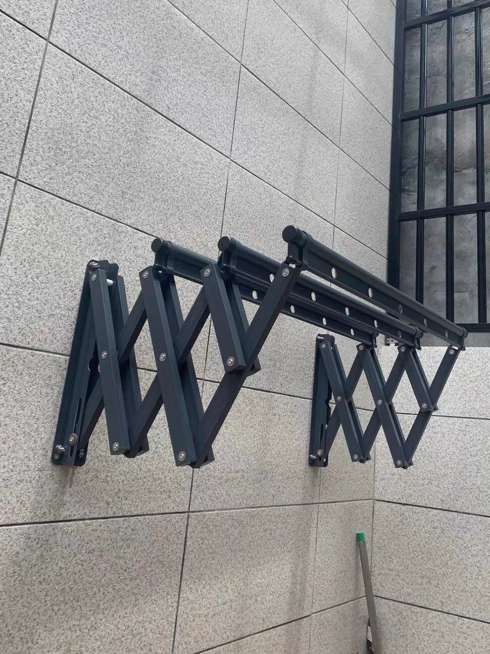 Real customer installation of a black EaseRack retractable drying rack on a balcony wall.