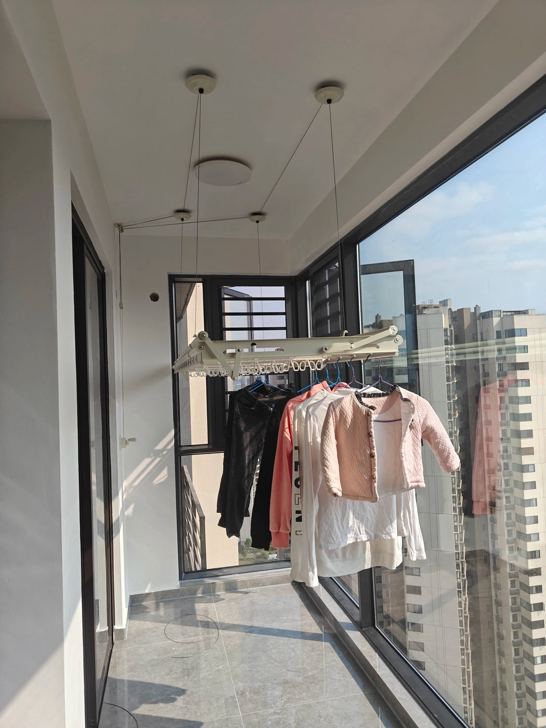 Ceiling clothes airer installed on an enclosed balcony with everyday clothes hanging below