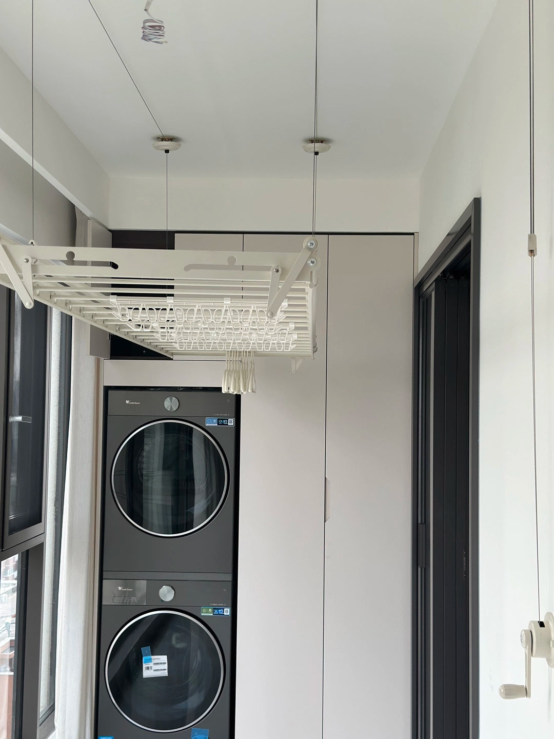 Ceiling clothes airer installed above a washer and dryer with the wall-mounted hand crank visible