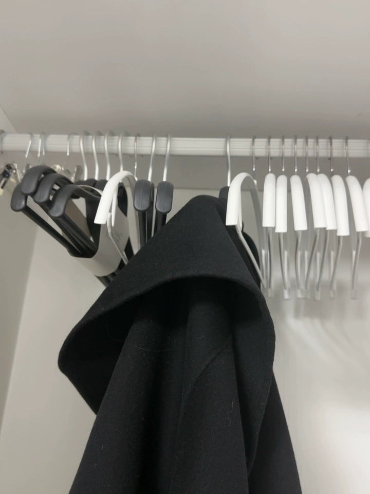 Wide-shoulder no-mark clothes hanger holding a black coat on a closet rod