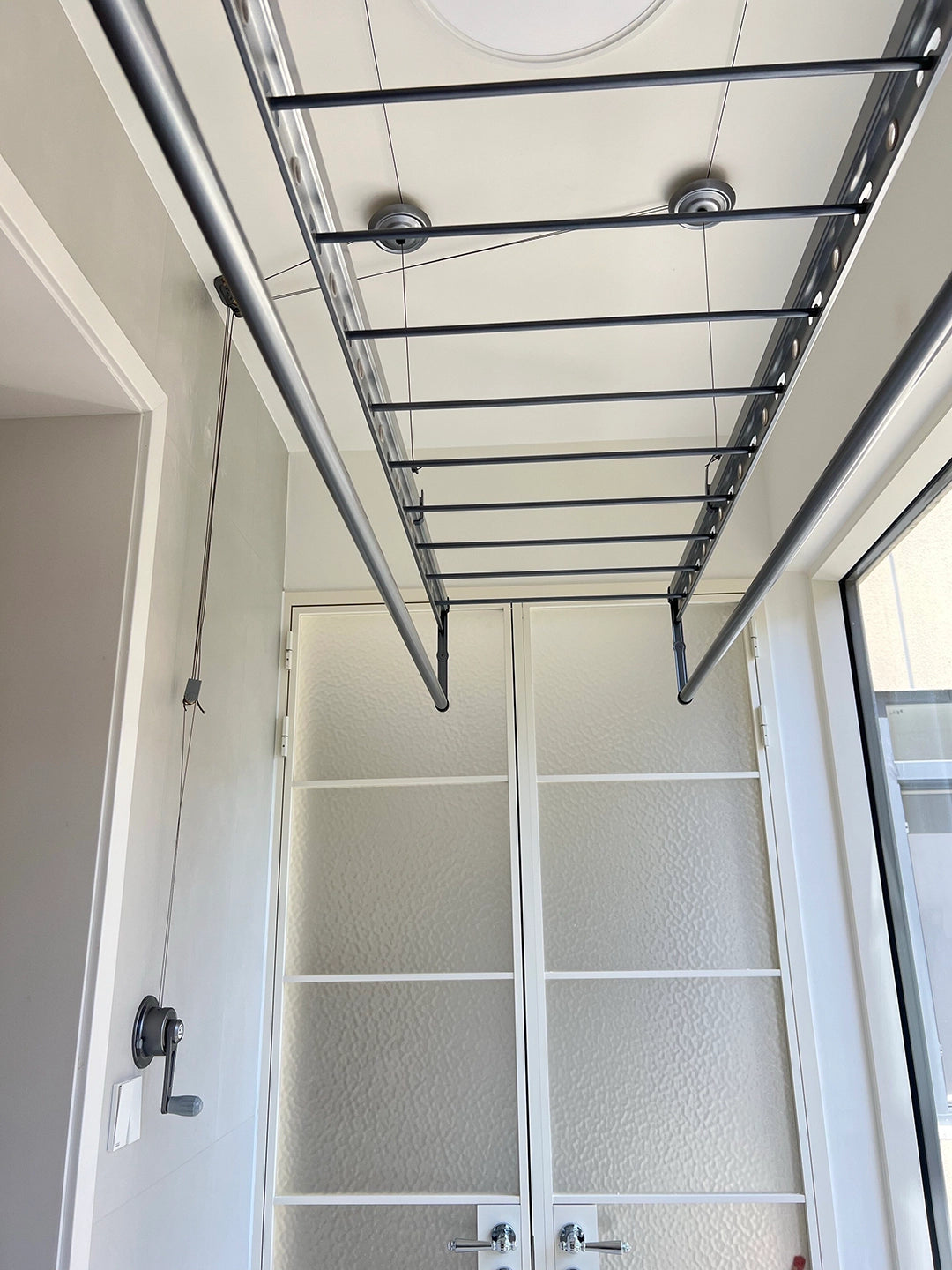 Square-Rod ceiling clothes airer installed in an enclosed balcony with a wall-mounted manual winch